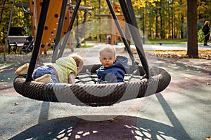 Two scared toddlers boy and girl left unattended are sitting on a swing hammock on a playground in the autumn park
