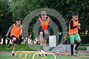 Two school boys are running ladder drills on the turf during football summer camp. Intense soccer training with coach.