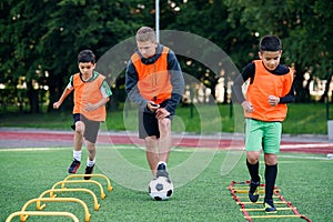 Two school boys are running ladder drills on the turf during football summer camp. Intense soccer training with coach.