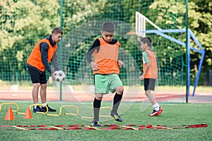 Two school boys are running ladder drills on the turf during football summer camp. Intense soccer training with coach.