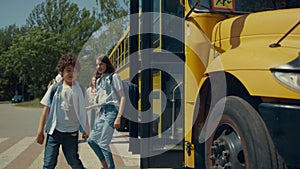 Two school children going out schoolbus. Teenagers standing at bus talking.