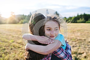 Two school children walking on field trip in nature, hugging.