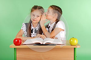 Two school girl sharing secrets sitting at a desk from book