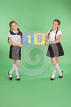 Two school girls hold color board with the number eighteen