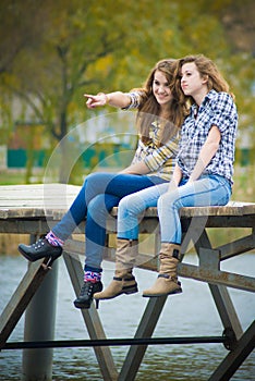 Two school girls sitting on river bridge