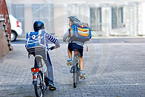 Two school kid boys in safety helmet riding with bike in the city with backpacks. Happy children in colorful clothes