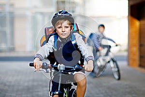 Two school kid boys in safety helmet riding with bike in the city with backpacks. Happy children in colorful clothes
