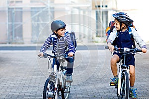 Two school kid boys in safety helmet riding with bike in the city with backpacks. Happy children in colorful clothes