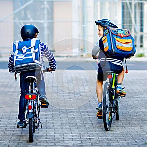 Two school kid boys in safety helmet riding with bike in the city with backpacks. Happy children in colorful clothes