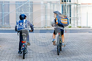 Two school kid boys in safety helmet riding with bike in the city with backpacks. Happy children in colorful clothes