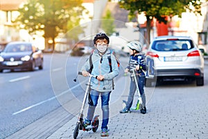 Two school kid boys in safety helmet riding with scooter in the city with backpack on sunny day. Happy children in