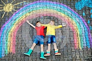 Two school kids boys having fun with with rainbow picture drawing with colorful chalks on asphalt. Siblings, twins and