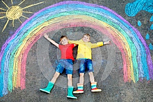 Two school kids boys having fun with with rainbow picture drawing with colorful chalks on asphalt. Siblings, twins and