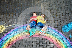 Two school kids boys having fun with with rainbow picture drawing with colorful chalks on asphalt. Siblings, twins and