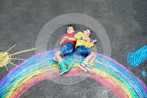 Two school kids boys having fun with with rainbow picture drawing with colorful chalks on asphalt. Siblings, twins and