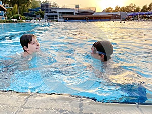 Two school kids boys playing and splashing in an outdoor swimming pool on warm summer day. Happy healthy children