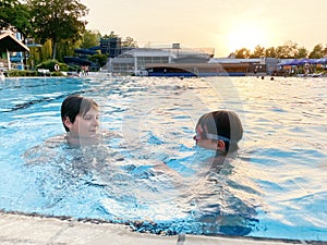 Two school kids boys playing and splashing in an outdoor swimming pool on warm summer day. Happy healthy children