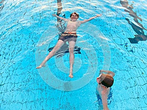 Two school kids boys playing and splashing in an outdoor swimming pool on warm summer day. Happy healthy children