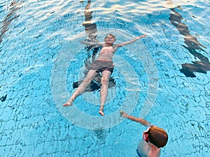 Two school kids boys playing and splashing in an outdoor swimming pool on warm summer day. Happy healthy children