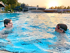 Two school kids boys playing and splashing in an outdoor swimming pool on warm summer day. Happy healthy children