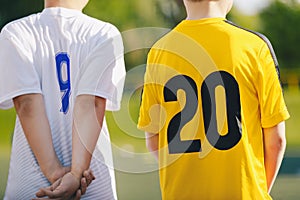 Two school kids in sporty jersey shirts with numbers on the backside