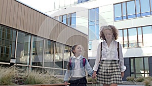 Two schoolgirls of different ages with backpacks go to school, holding hands. The older sister takes the younger one to