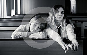 Two schoolgirls seated at desk in uniform in a classroom. One is an Asian girl who appears to be asleep while the other, a