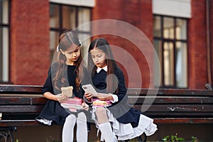 Two schoolgirls is sitting outside together near school building