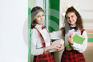 Two schoolgirls are standing in the hallway with books