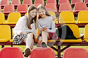 Two schoolgirls watch videos together on a smartphone in the school stands. The concept of friendship and relationships