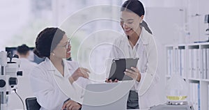 Two scientists high five while using a digital tablet in a laboratory. Happy female doctors celebrate an achievement