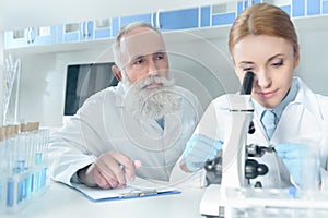 Two scientists in white coats working together with microscope