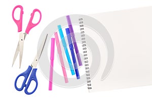 Two scissors, five felt tip pens in pink, blue and purple colors and blank sketchbook, isolated on white background. Space for tex