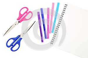 Two scissors, five felt tip pens in pink, blue and purple colors and blank sketchbook, isolated on white background. Space for tex