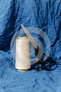 two scissors and thread on a blue cloth background with a pair of scissor