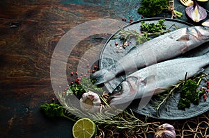 Two sea bass fish with spices on a black stone plate. On a dark background.