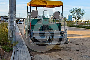 Two-seater asphalt paving machine, open car with awning and yellow fabric roof. the asphalt paving bucket is installed at the rear