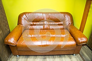 A two-seater faux leather sofa with brown armrests against a yellow wall. Interior furniture living