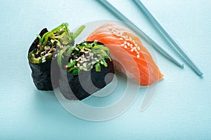 Two seaweed Sushi Chuka and sushi nigiri with salmon with chopsticks on a blue