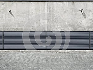 Two security cameras hanging on the concrete wall of the building, aimed at the space behind the fence