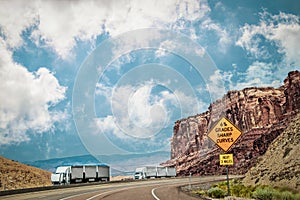 Two semi trailer trucks withthree trailers each - one broken down in canyonlands of Utah USA with sign 6% grades and sharp curves