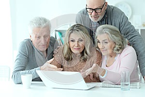 Two senior couples sitting at table and looking at laptop