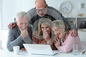 two senior couples sitting at table and using laptop