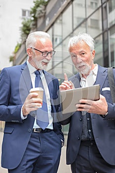 Two senior gray haired businessmen talking in front of an office building