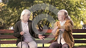 Two senior ladies arguing and sitting on bench in park, grumpy elders, dispute
