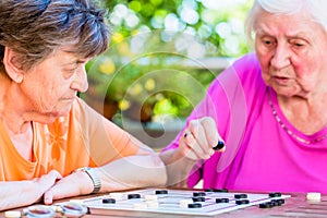 Two senior ladies playing board game in rest home