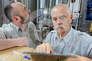 Two senior men in brewery using digital tablet