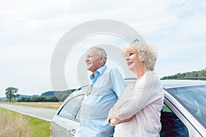 Two senior people smiling with confidence while leaning on their car