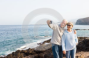 Two senior people take a selfie on the cliff of the ocean.Hugging and smiling. Morning soon outdoor with clear sky. Vacation and