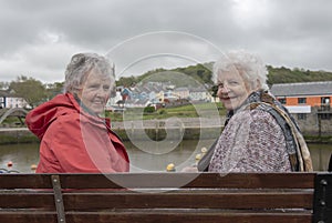 Two senior woman sitting on a park bench outdoors